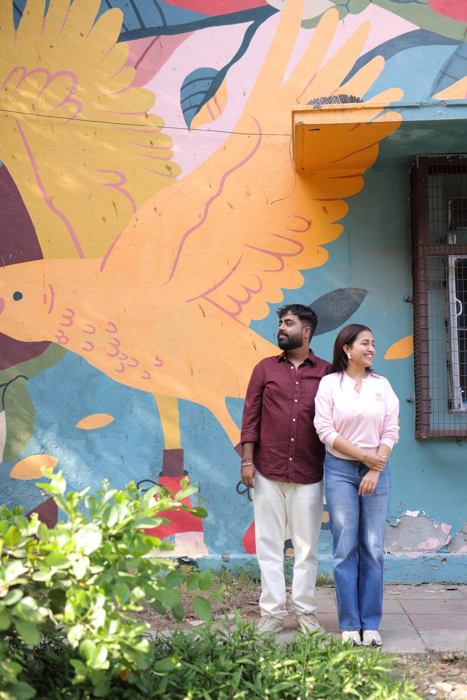 Disha and Mayank in front of a painted bird mural