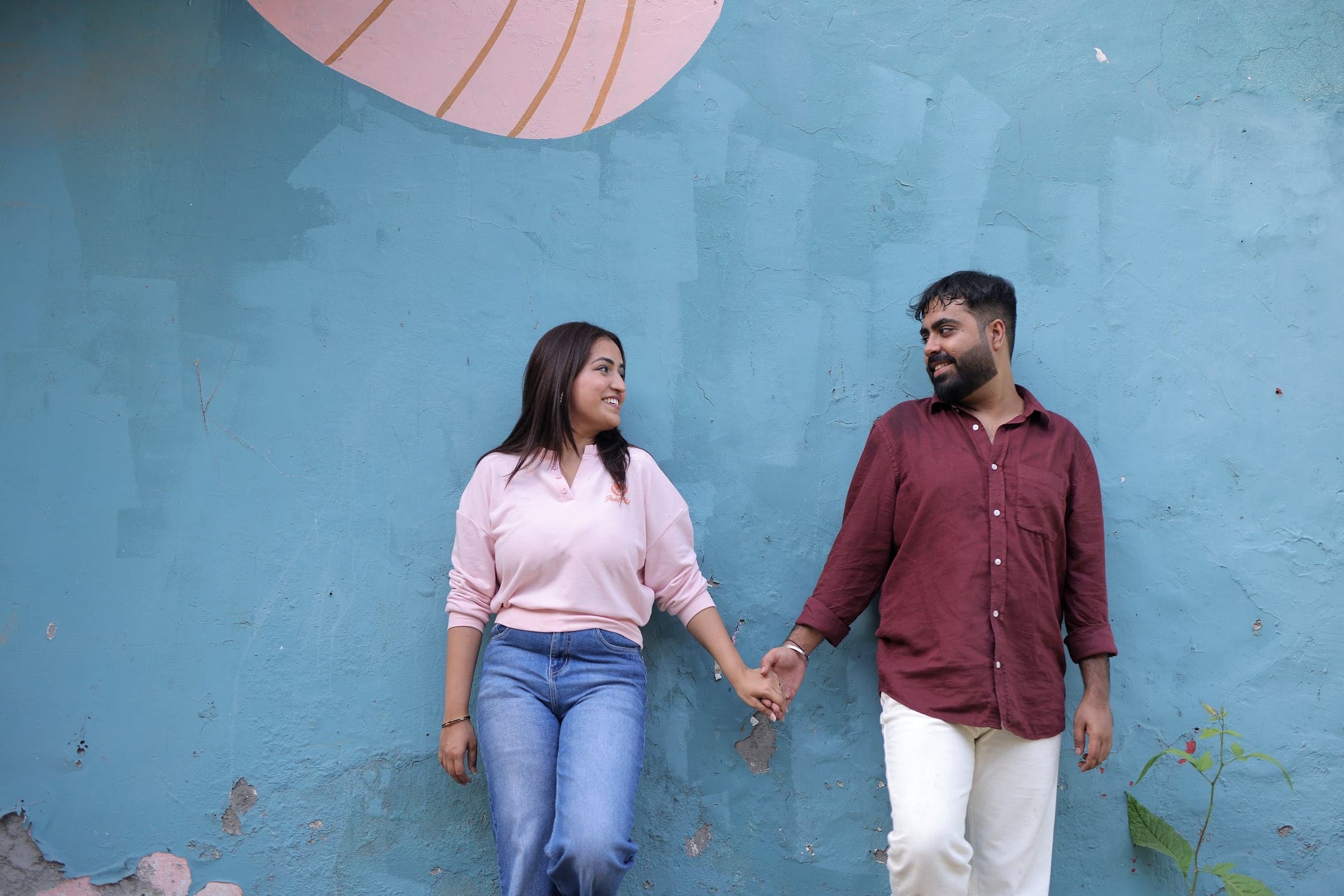 Disha and Mayank holding hands against a blue wall